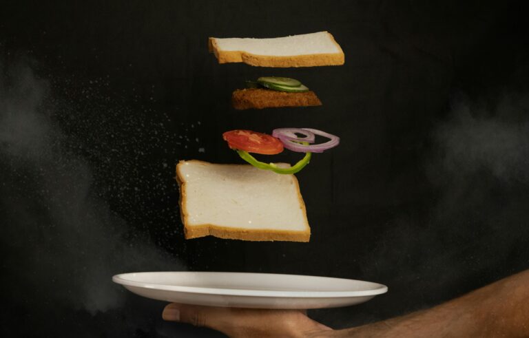 Creative composition of a sandwich with floating ingredients against dark background.